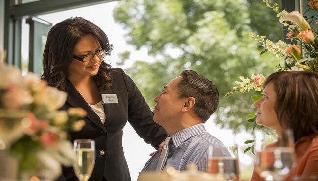 A female Dignity Memorial associate smiles as she talks to an Asian man with her hand on his shoulder. 