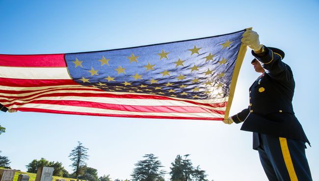 A man in uniform holds an American flag and performs military honors