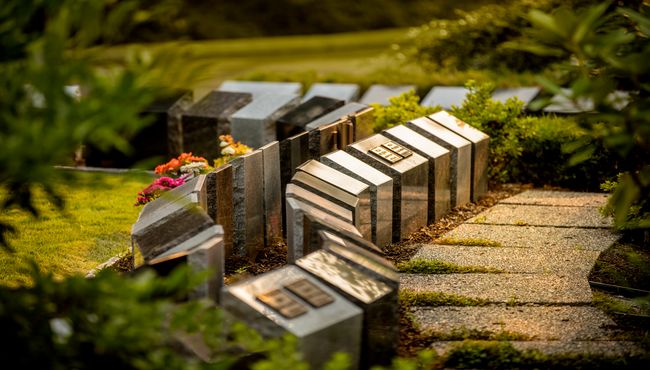 A walkway weaves through natural landscaping along a row of cremation monuments with plaques at Boal Memorial Gardens.