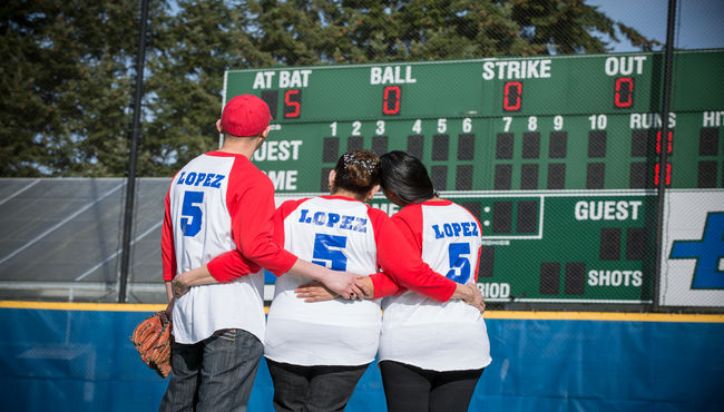 Three teammates hug, wearing matching commemorative baseball jerseys.