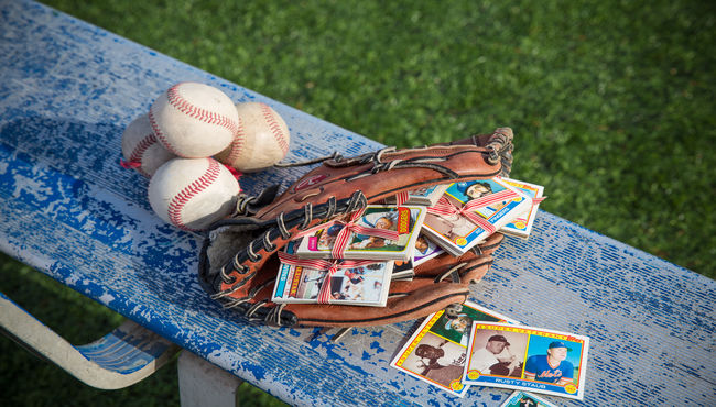 Glove full of baseball cards on a bench nest to a pile of baseballs