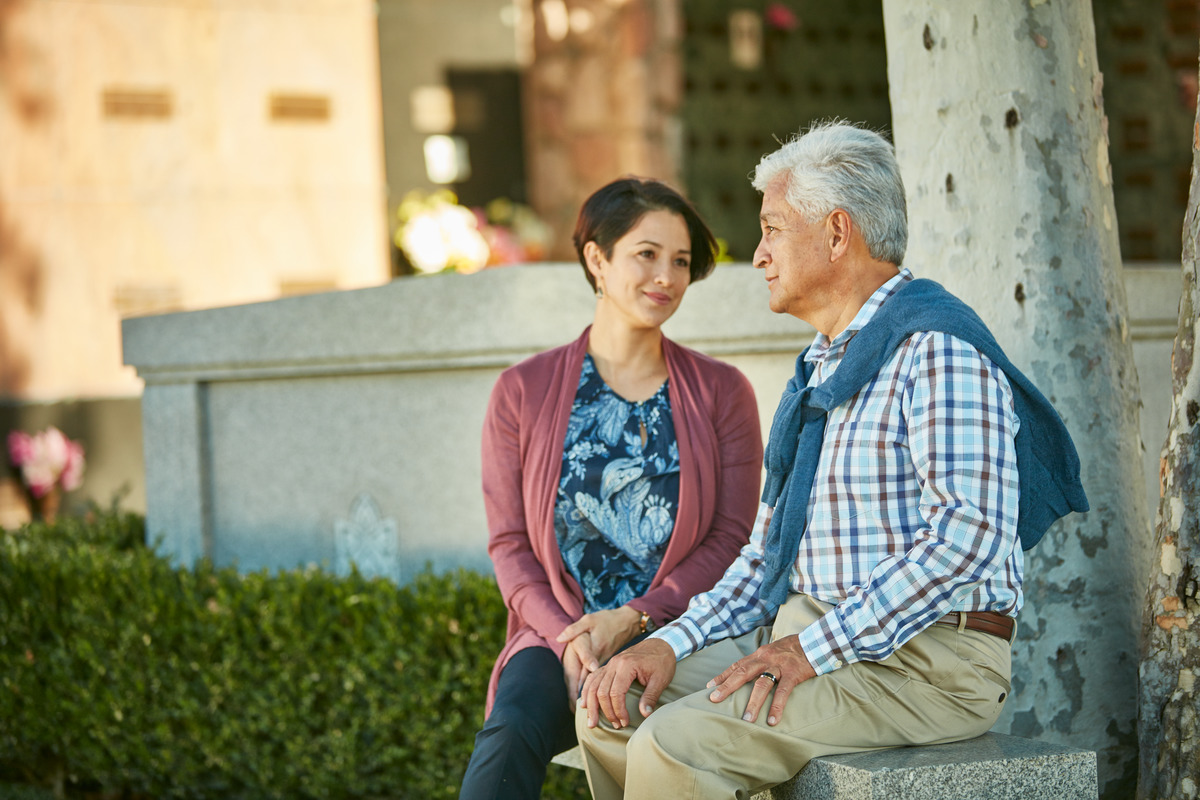 Family members comfort one another while resting on a bench near a community mausoleum.