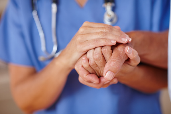 Medical professional comforting another person by holding their hand.
