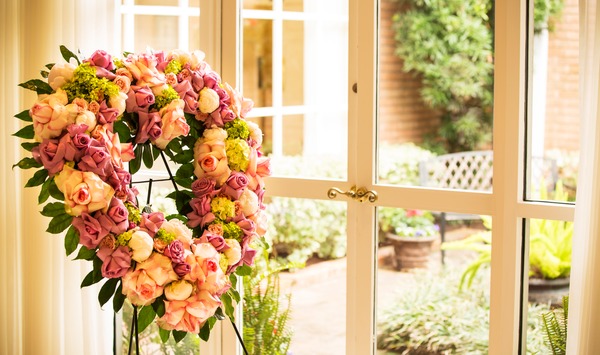 Rose floral heart-shaped wreath on stand facing window.
