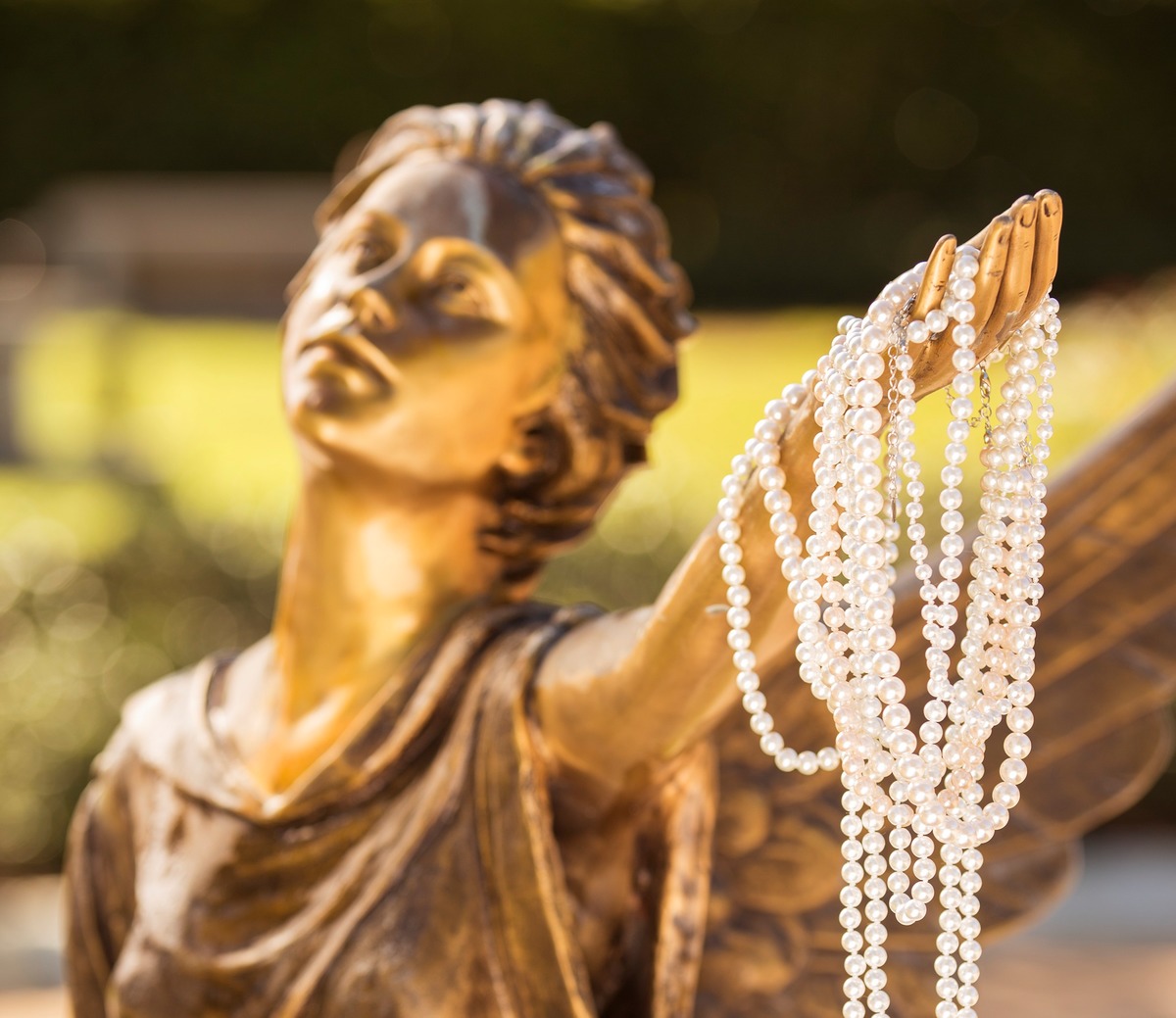 Une statue d'ange ailé en bronze tenant un collier de perles.