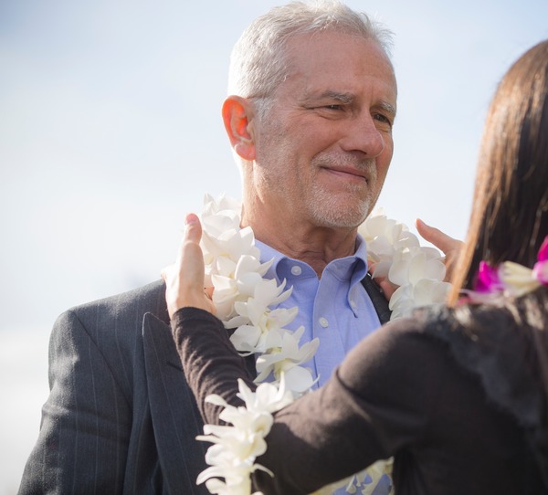 Woman puts Hawaiian lei around a man's neck at an outdoor memorial