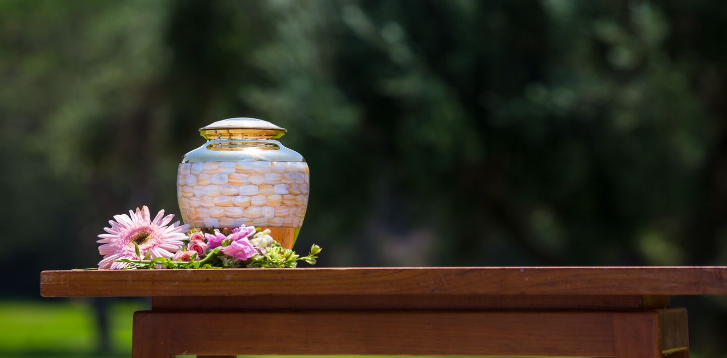 Urn outside on table with flowers around it