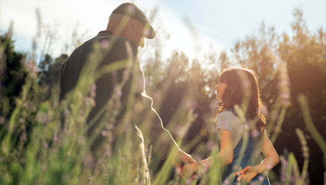 Grandfather and granddaughter holding hands in field