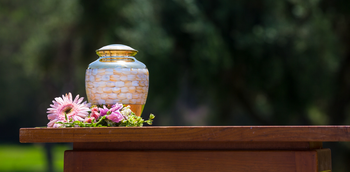 Urn outside on table with flowers around it